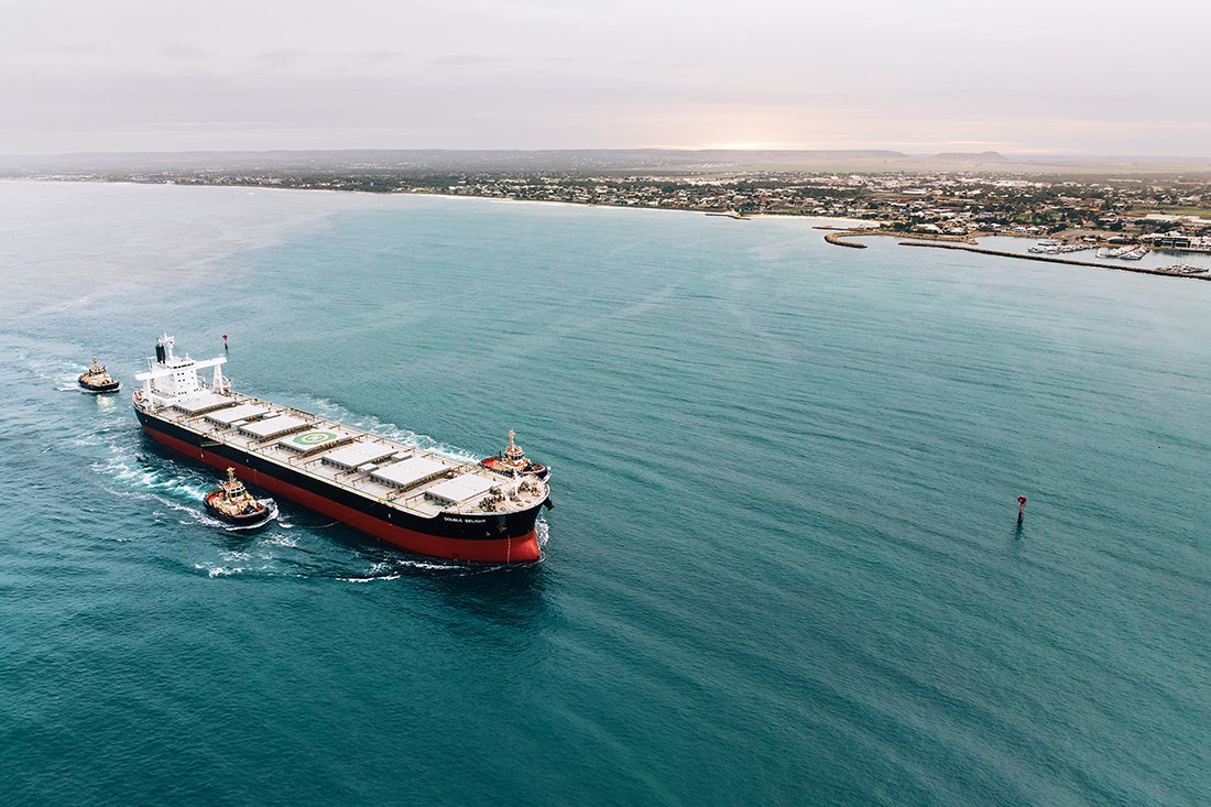 A Cargo ship entering the port with 3 tug boats accompanying it.